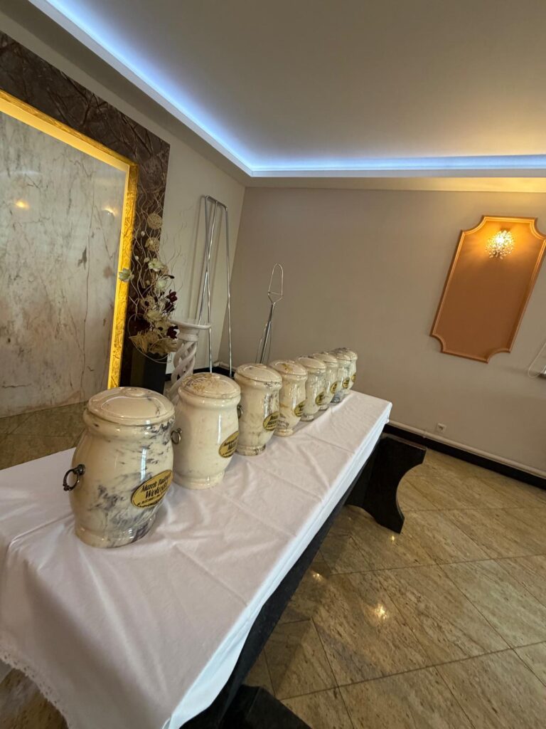 Rząd jasnych, kamiennych urn z prochami donatorów przygotowanych do uroczystej ceremonii pożegnalnej w sali domu pogrzebowego.