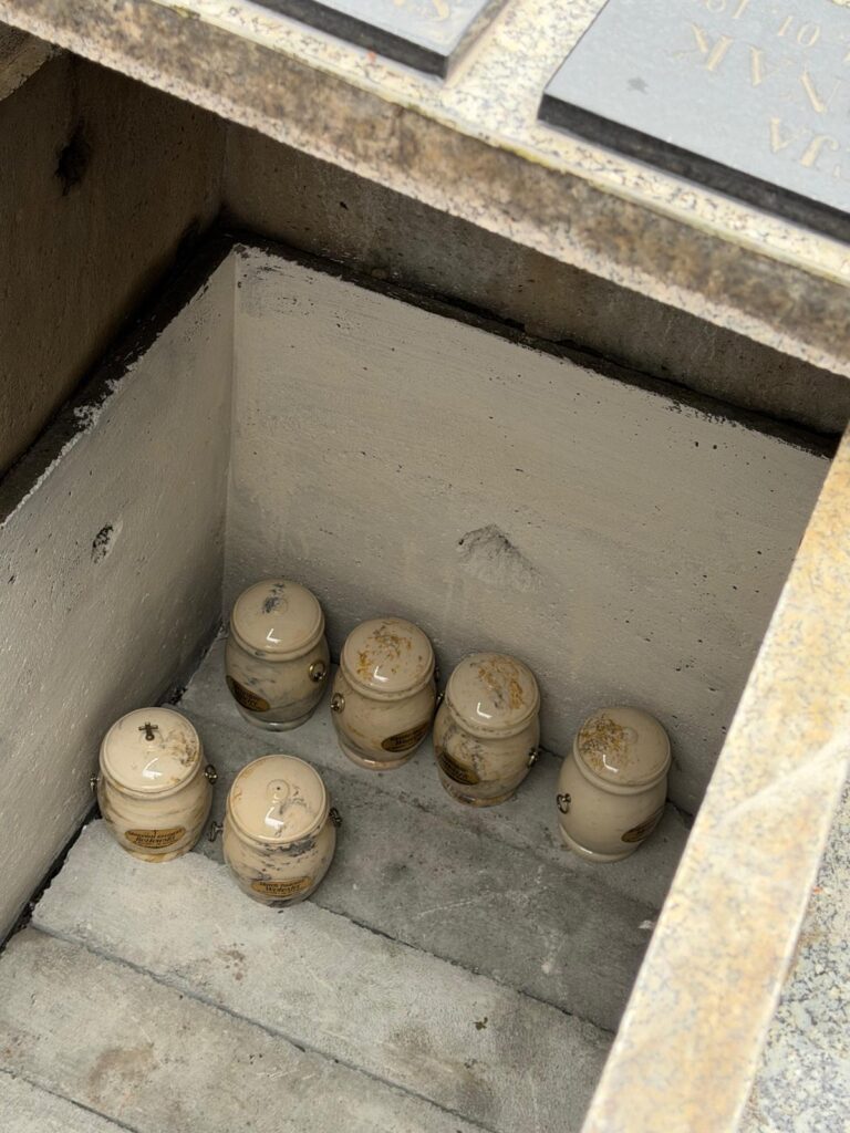 Jasne urny z prochami donatorów umieszczone wewnątrz wspólnej krypty podczas uroczystości pogrzebowej. Widok z góry na wnętrze miejsca pochówku.