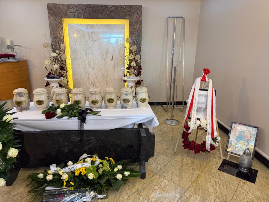 Uroczysta świecka ceremonia pożegnania donatorów ciała w sali pogrzebowej. Rząd urn z prochami na stole z białym obrusem, wieniec z szarfą od Uniwersytetu Medycznego w Lublinie oraz portret donatora, Marka Wołoskiego z Rybnika.
