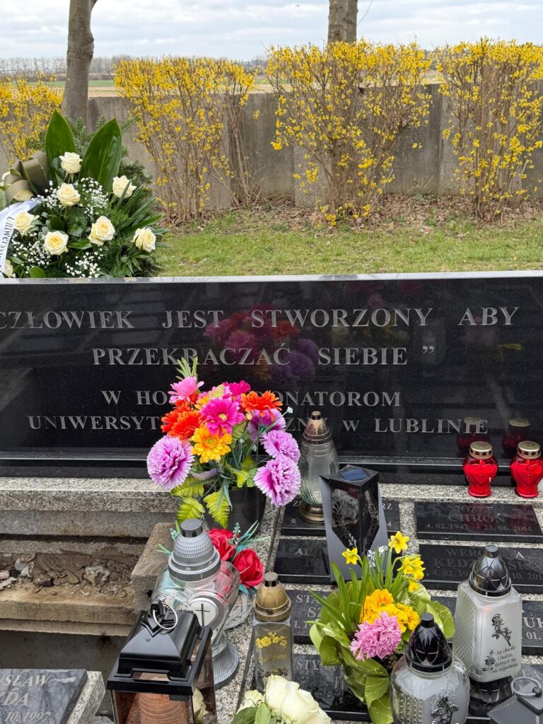 Zbliżenie na pomnik wspólnej mogiły donatorów z cytatem „Człowiek jest stworzony, aby przekraczać siebie”. Widoczne tablice pamiątkowe, znicze i kwiaty na kwaterze Uniwersytetu Medycznego w Lublinie.